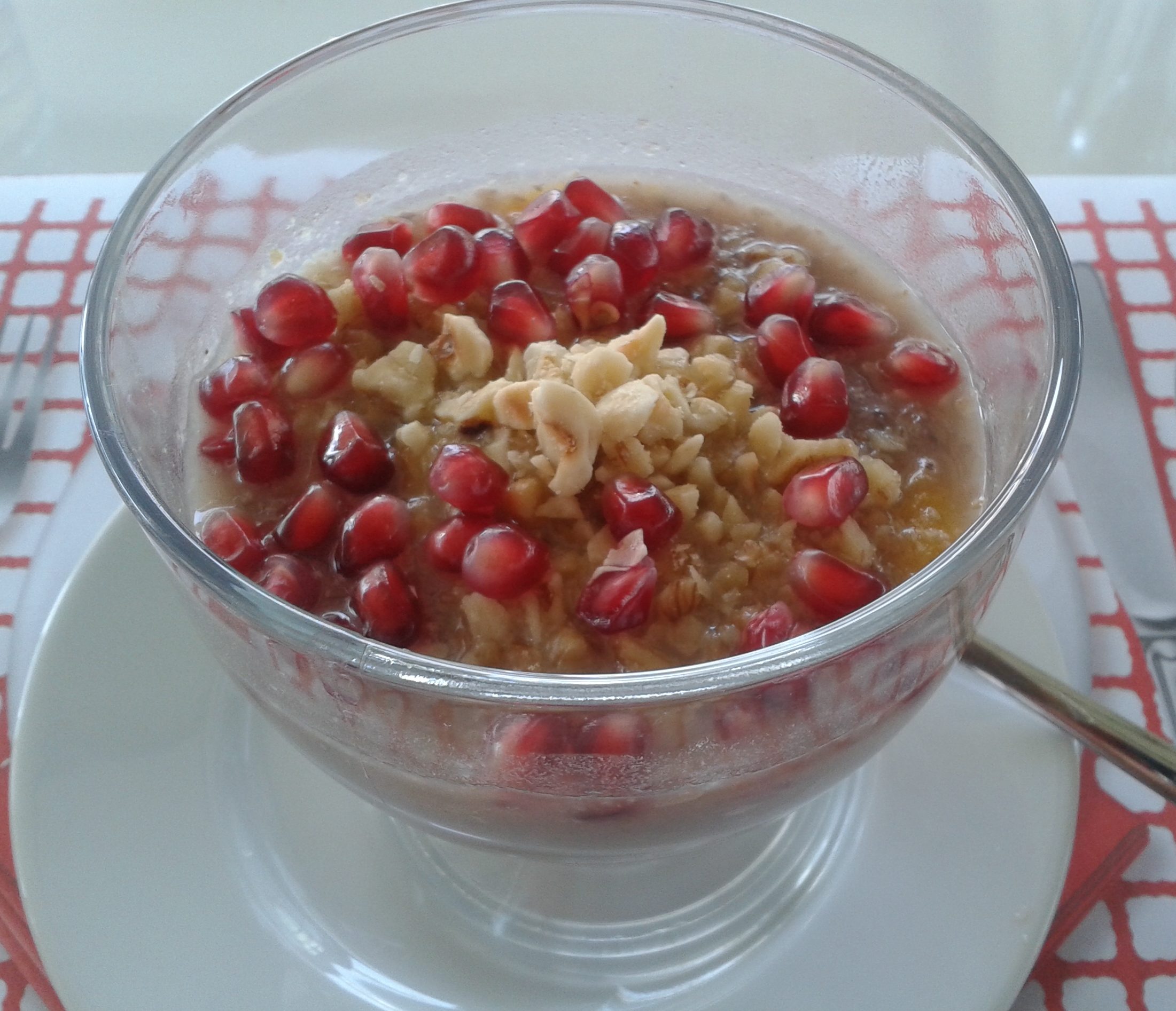 Close up of a dessert porridge with grains and nuts topped with pomegranate seeds.